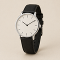 Reloj minimalista con esfera clara y correa negra sobre fondo beige